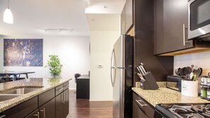 A modern kitchen with dark cabinetry, granite countertops, stainless steel appliances, and a cityscape artwork on the wall.