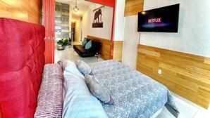 Ein modernes Schlafzimmer mit einem Bett, einem an der Wand montierten Fernseher und einer roten Tür zu einem weiteren Raum.