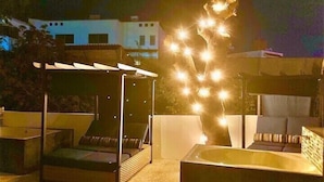 Eine Dachterrasse mit überdachter Sitzgelegenheit, einem Whirlpool und Lichterketten.