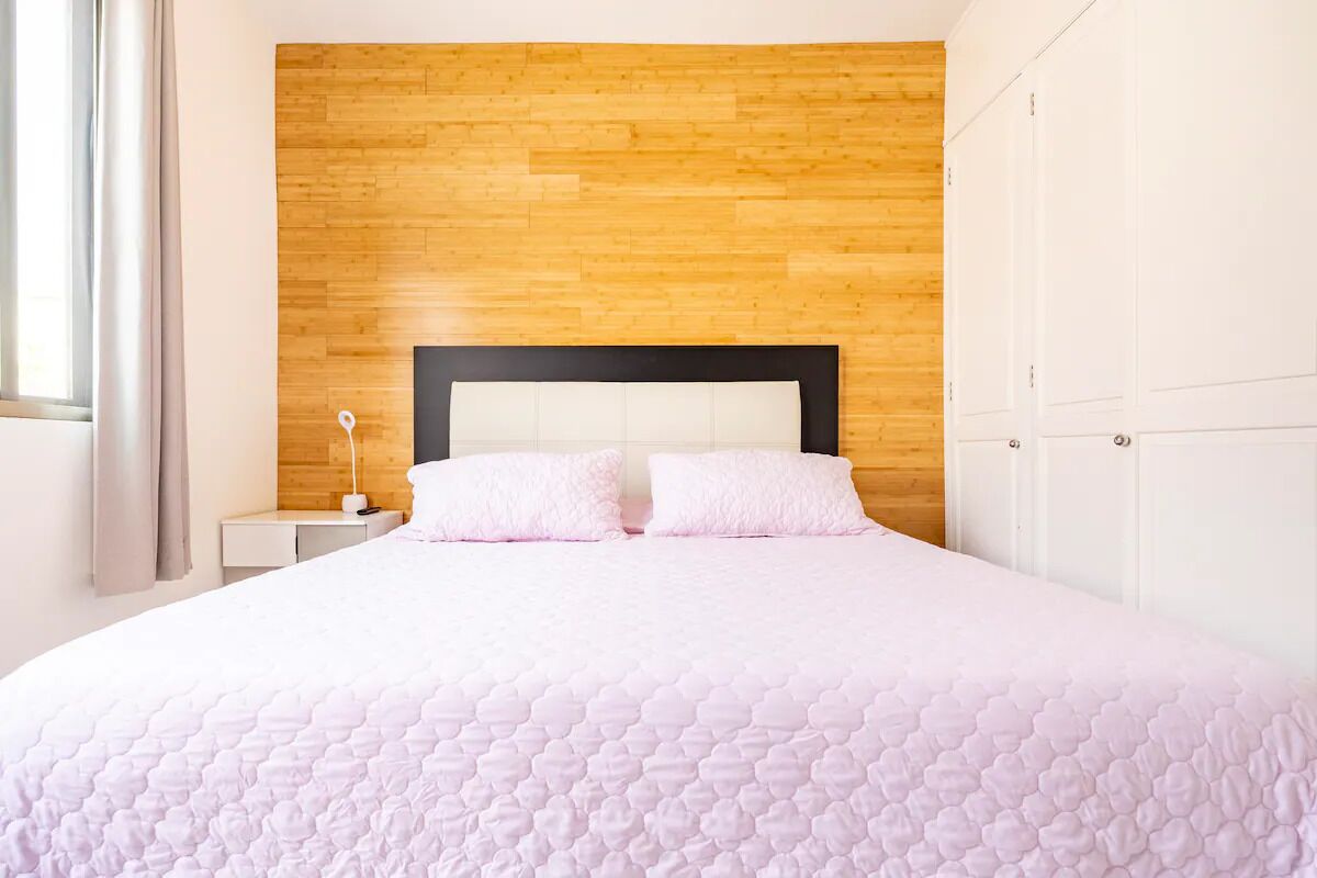A neatly made bed with a wooden headboard and white nightstands, a white wardrobe, and a window with curtains.