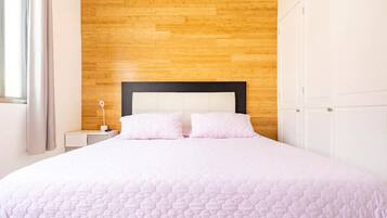 A neatly made bed with a wooden headboard and white nightstands, a white wardrobe, and a window with curtains.