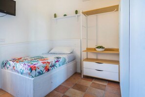 A small bedroom with a bed, a white dresser, a shelf with a plant, and a TV mounted on the wall.
