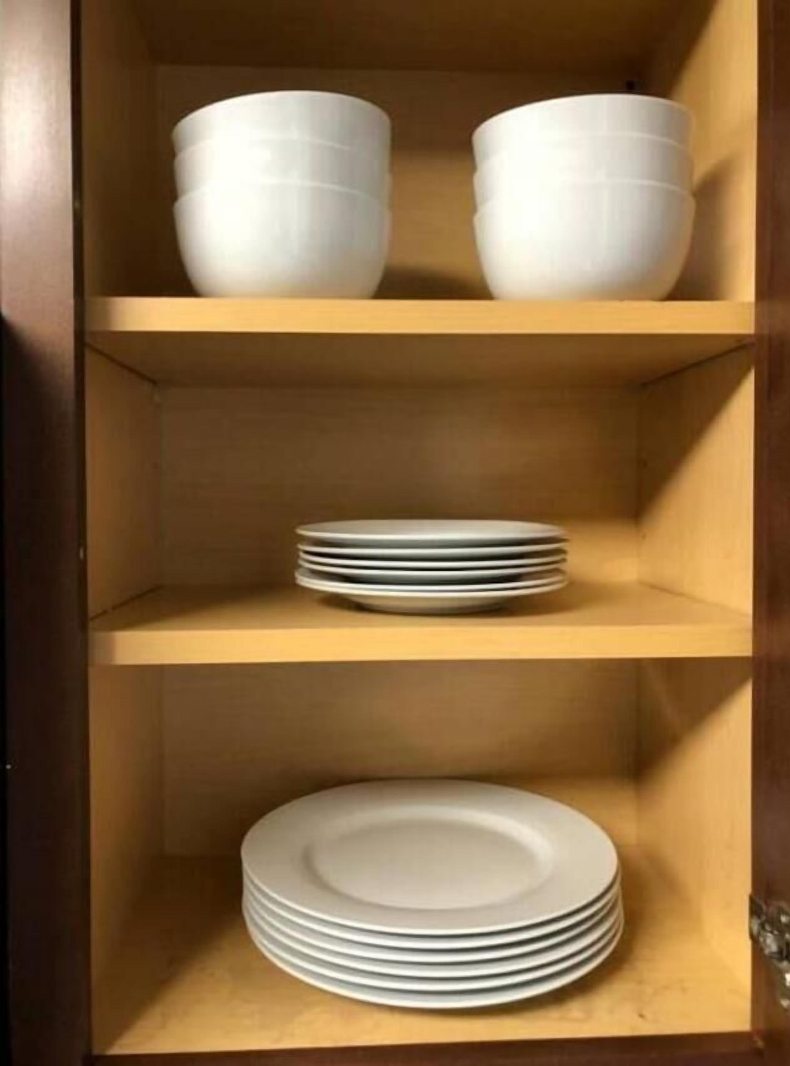A wooden cabinet with three shelves, each holding white bowls and plates.