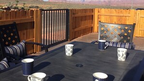 Eine Terrasse mit Esstisch für vier Personen, umgeben von einem Holzzaun, mit Blick auf eine Wüstenlandschaft.