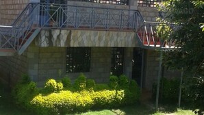 A building with a stone facade, a metal staircase, and a small garden with yellow flowers. - Taidy Suites Eldama Ravine (Eldama Ravine)