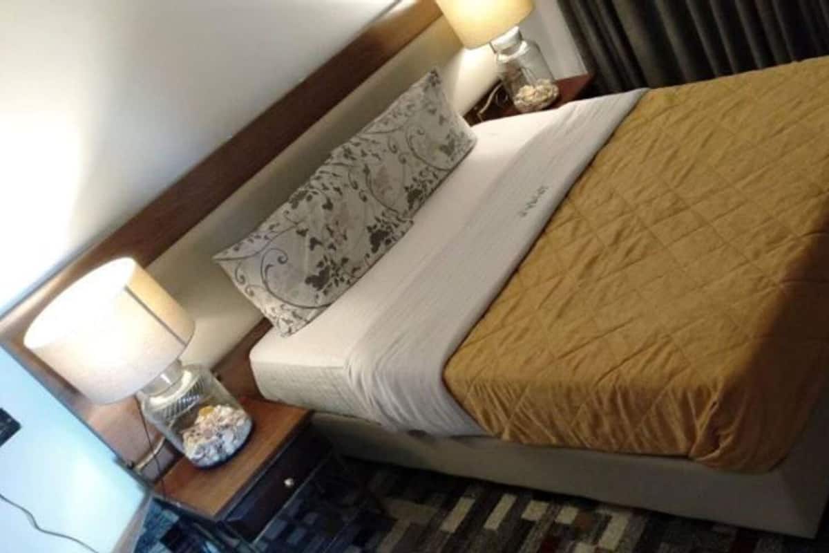 A neatly made bed with a patterned pillow and a brown blanket, a bedside lamp, and a small decorative jar on the nightstand.
