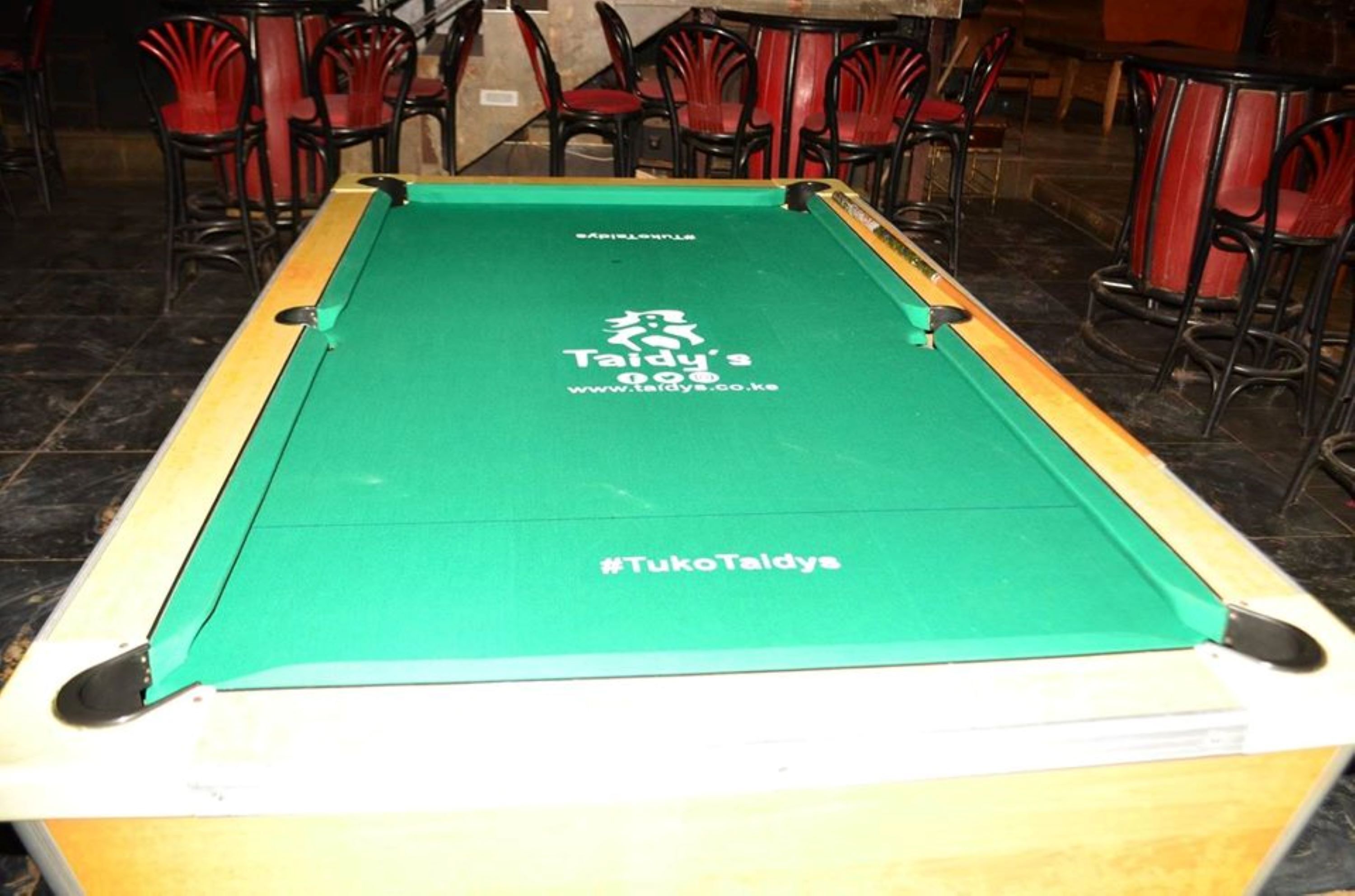 A pool table with a green felt surface, branded with "Taidy's" and the hashtag "#TukoTaidy's".