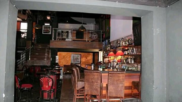 A bar area with wooden furniture, a counter with bottles, and a staircase leading to an upper level. - Taidy Suites Eldama Ravine (Eldama Ravine)