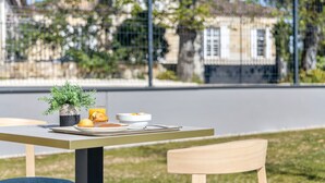 Una mesa con un tazón de cereal, un vaso de jugo de naranja y un muffin en un día soleado.