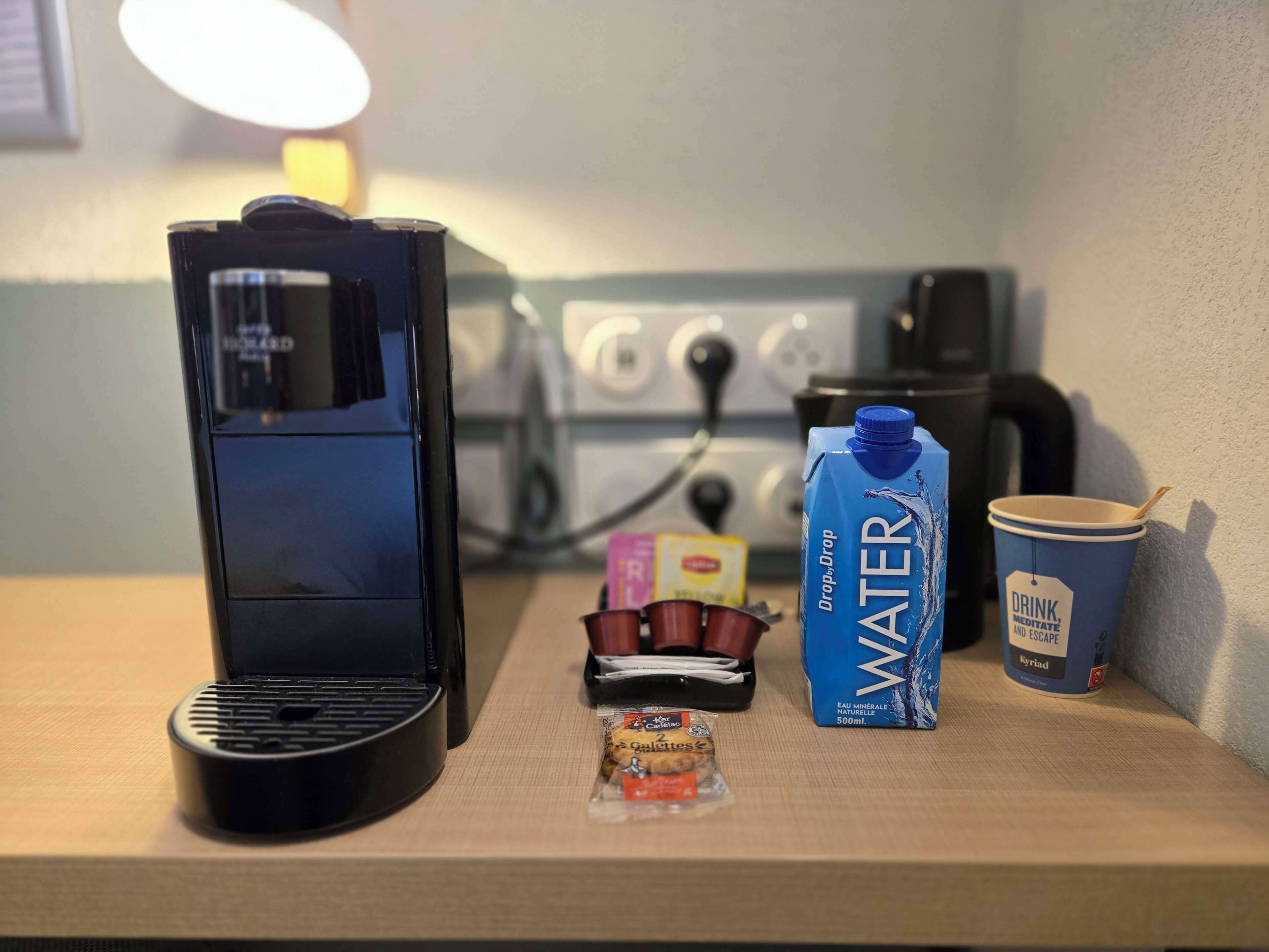 Een kitchenette met een koffiezetapparaat, een waterkan, een beker en een portie snacks.