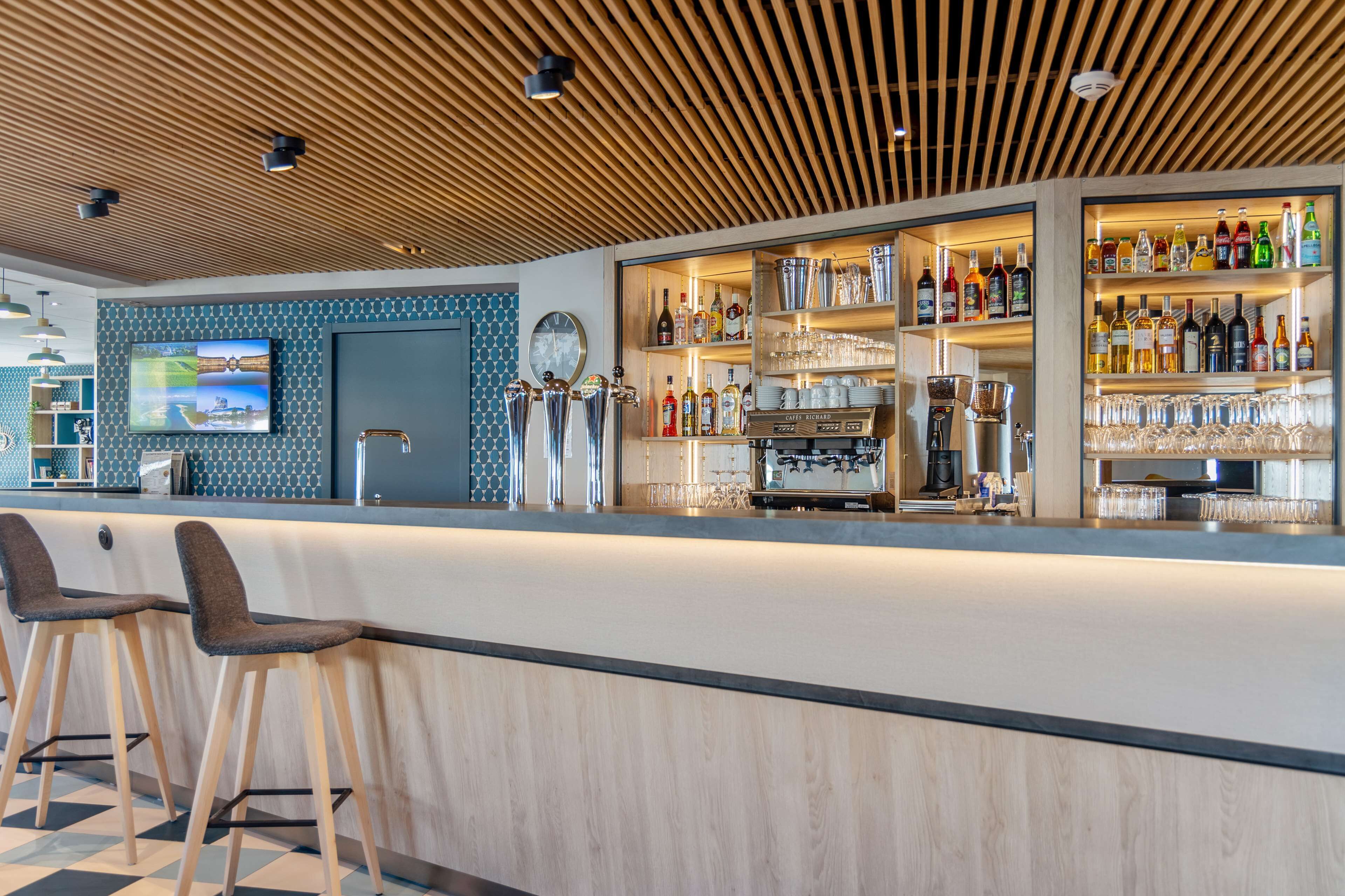 Eine moderne Bar mit Holzbalkendecke, Barhocker, einem Fernseher und einer gut sortierten Spirituosenregal.