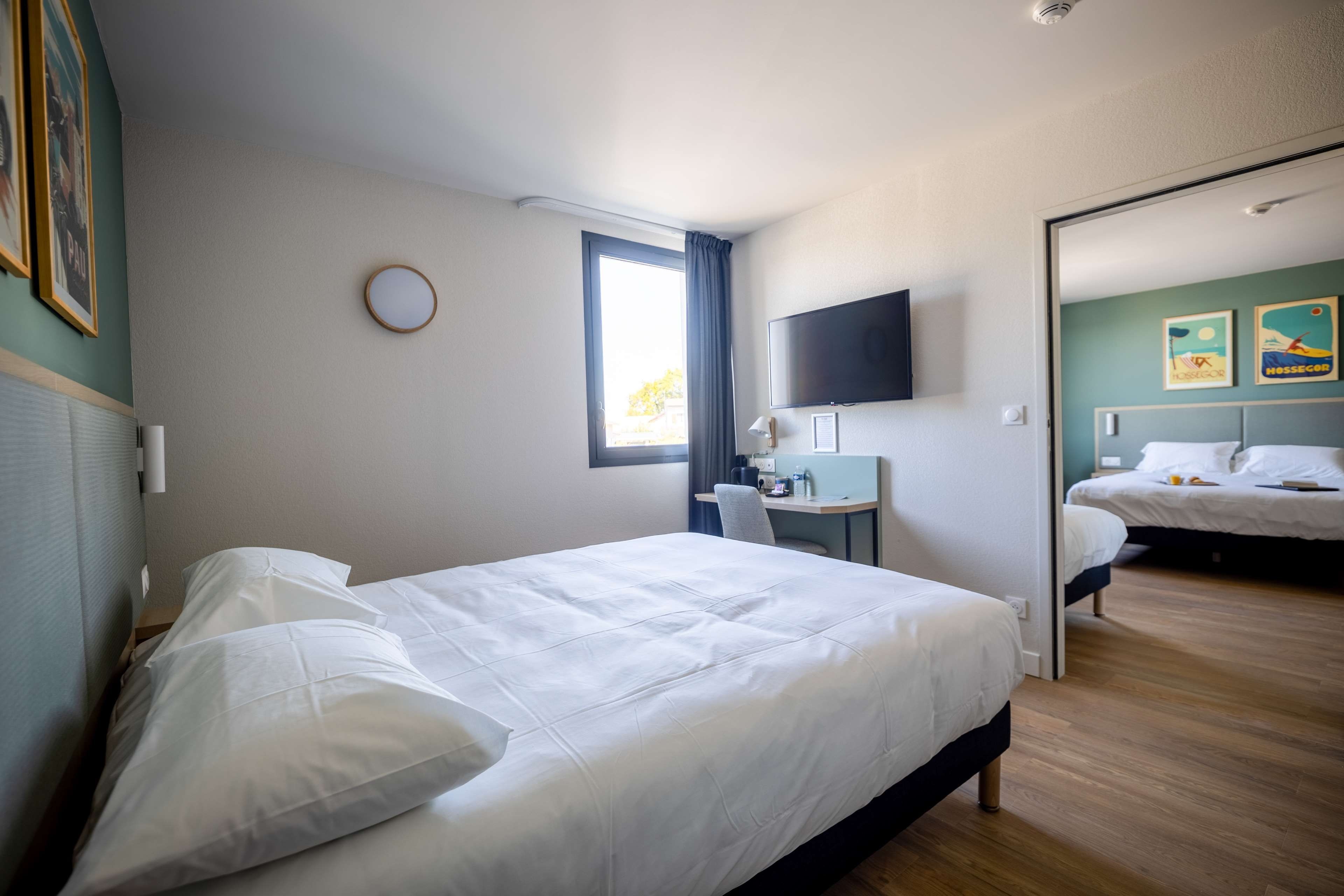 Habitación de hotel con cama, escritorio con silla, televisión y una segunda cama al fondo.