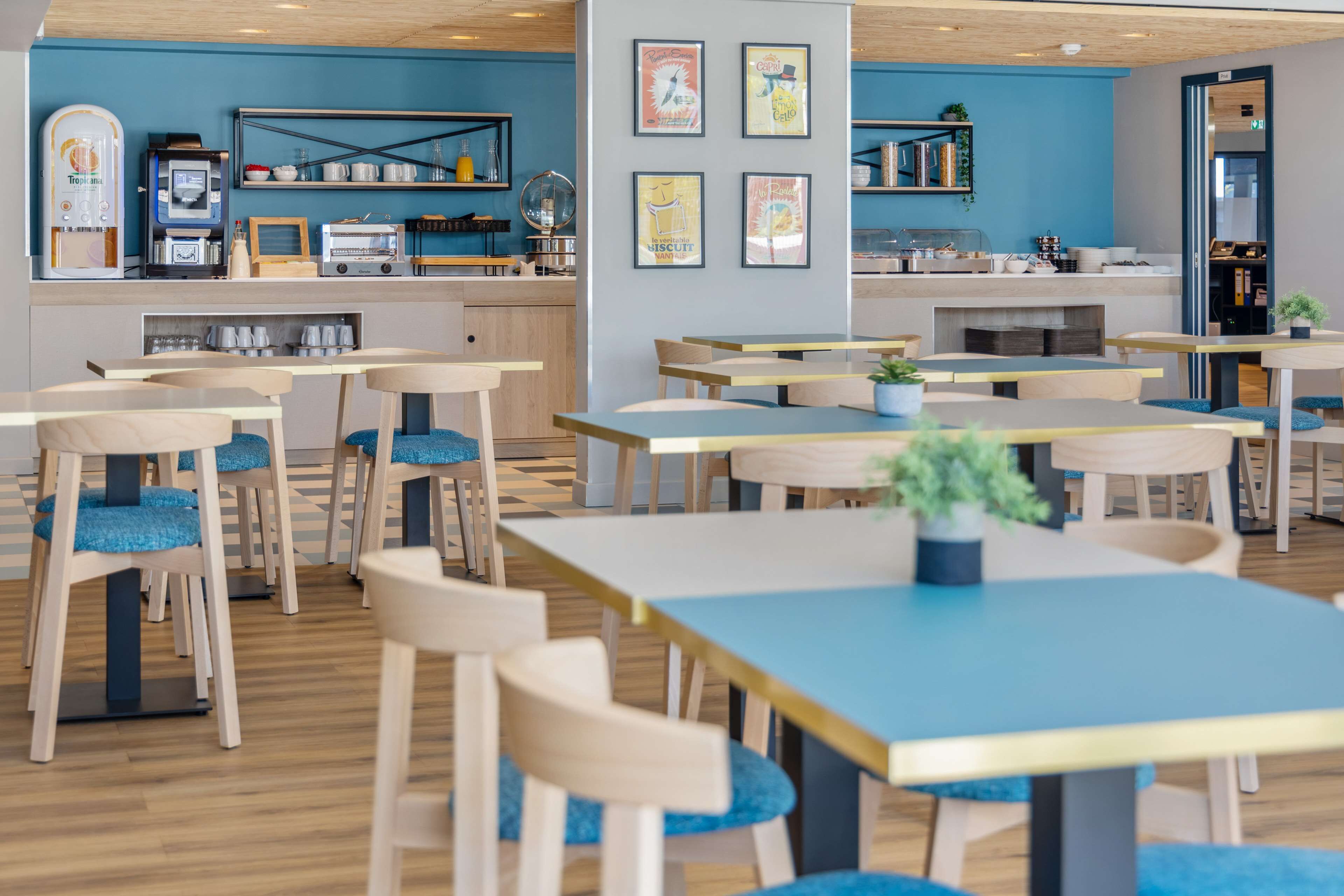 Un café moderno con mesas de madera y sillas con cojines azules, una máquina de café y una barra con diversos artículos.