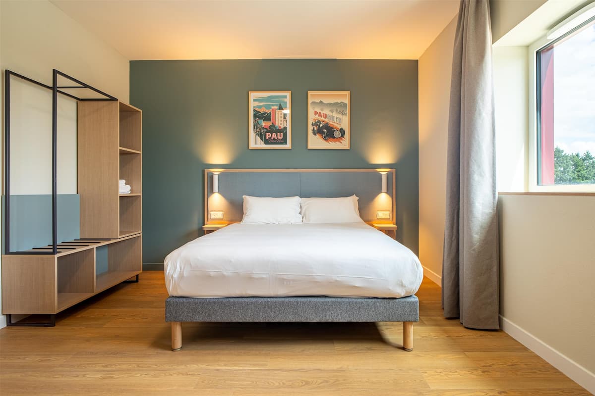 Une chambre à coucher moderne avec un lit, des lampes de chevet, une armoire en bois et deux tableaux encadrés accrochés au mur.