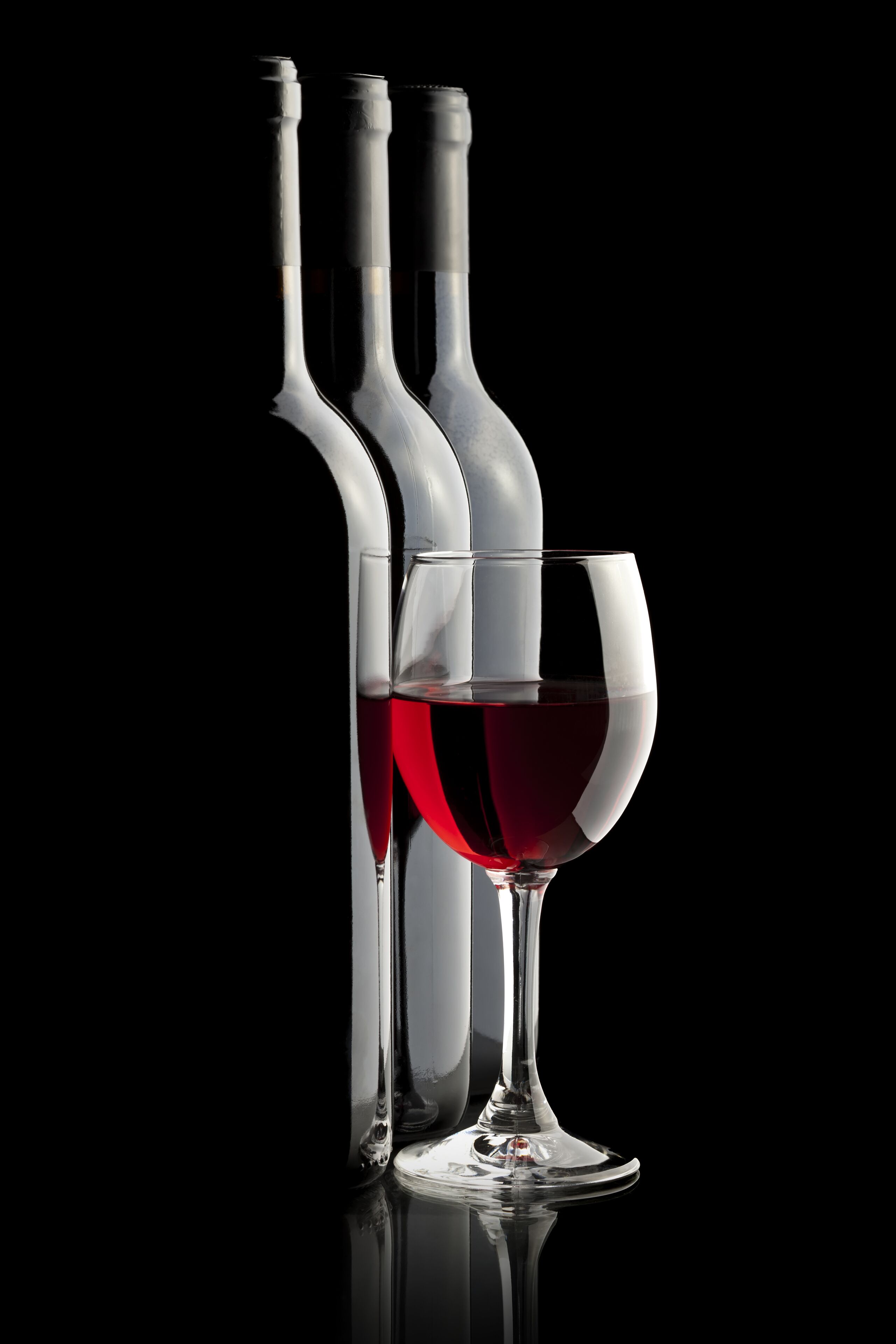 Three wine bottles and a wine glass against a black background.