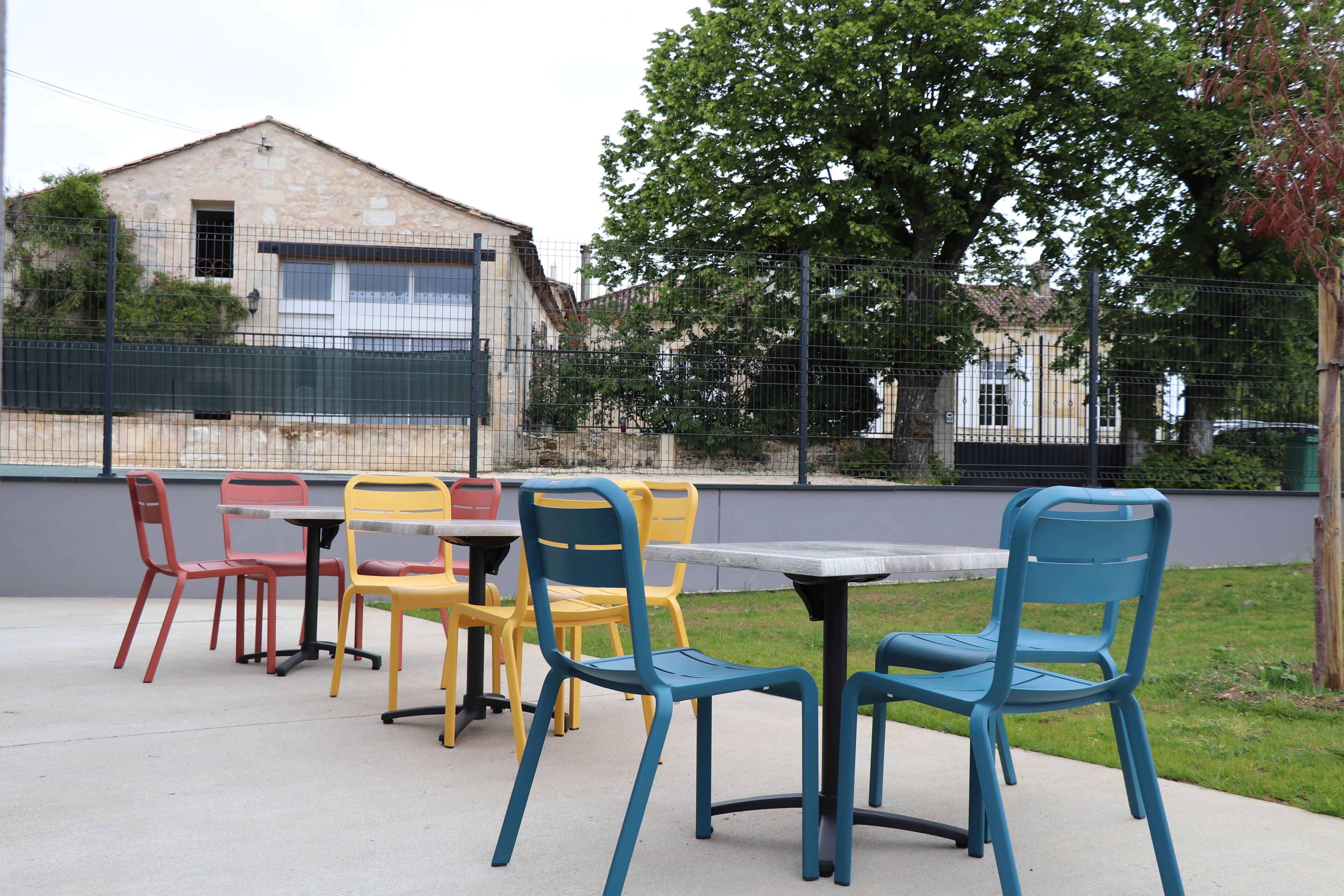 Un espace extérieur aménagé en terrasse avec une table et des chaises, un bâtiment en pierre en arrière-plan et une clôture.