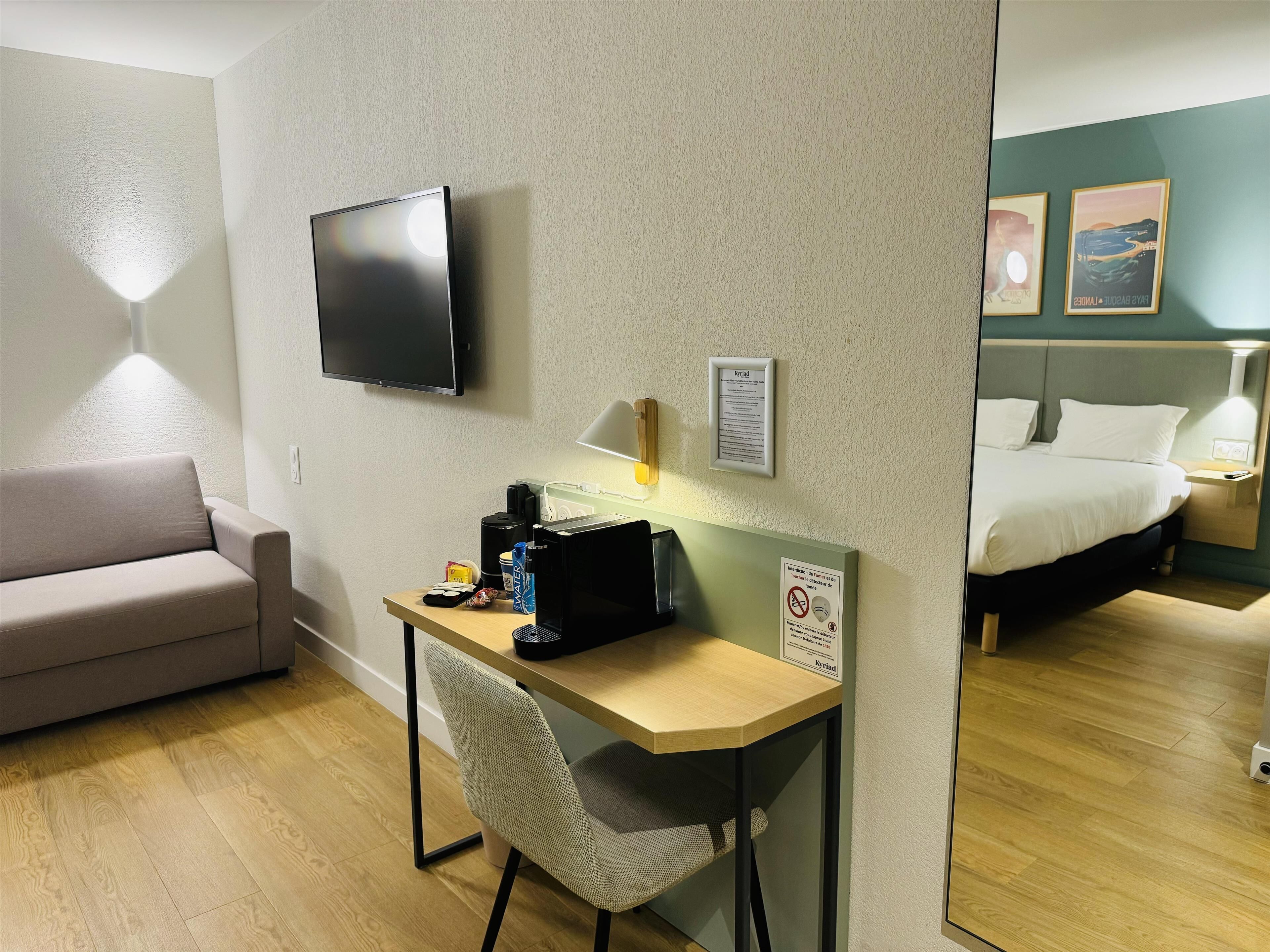 A hotel room with a desk, chair, flat-screen TV, bed, and artwork on the wall.