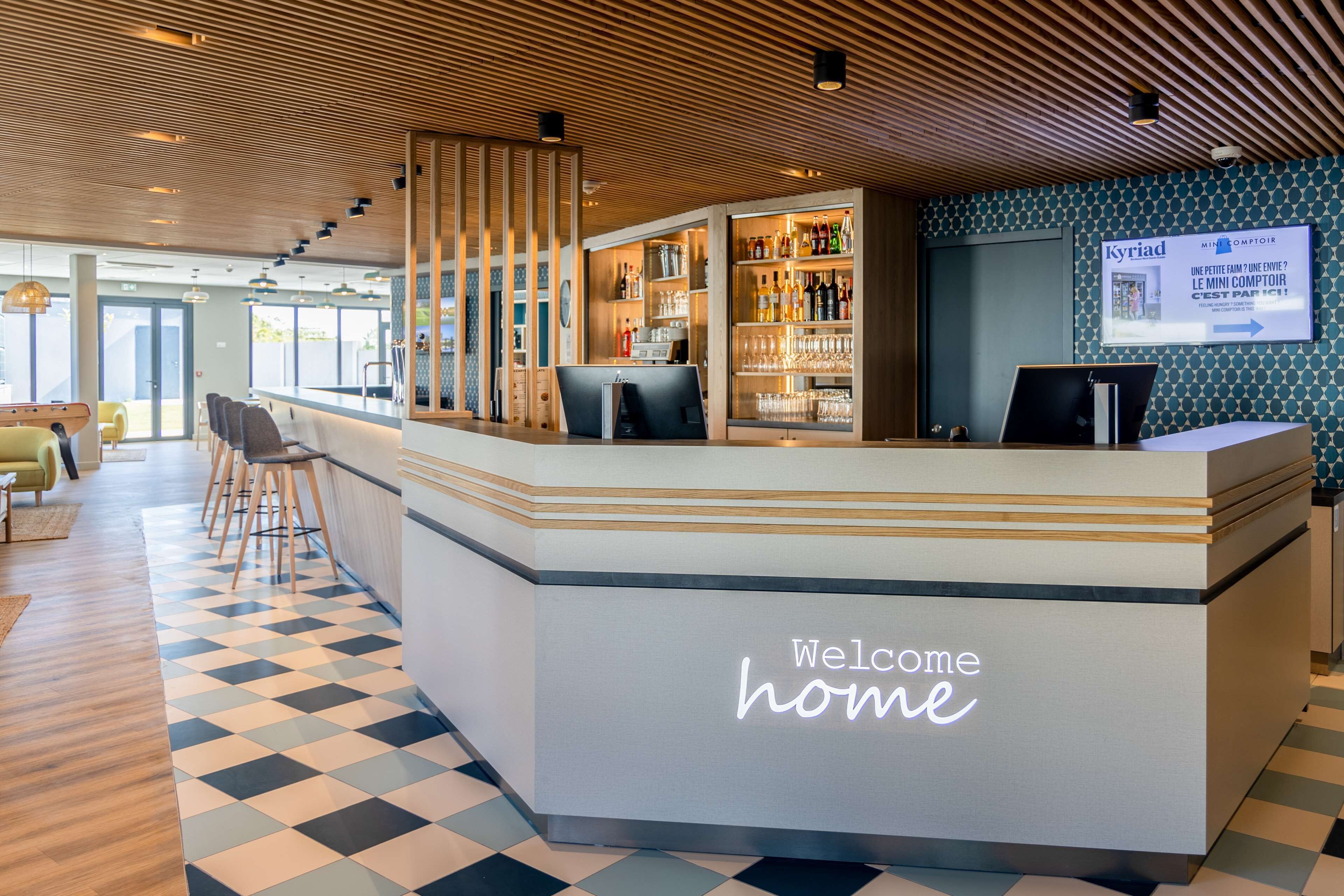 A reception area with a 'Welcome home' sign, a bar with various bottles, and a patterned floor.