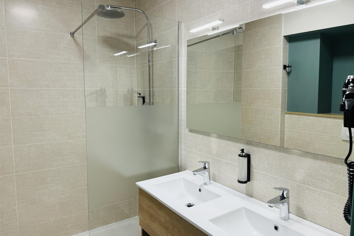 Une salle de bain moderne dotée d’une douche à parois de verre, d’un grand miroir et d’un meuble-lavabo en bois avec deux vasques.