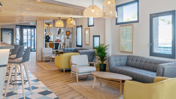 Un moderno vestíbulo de hotel con una recepción, zona de estar y grandes ventanales.