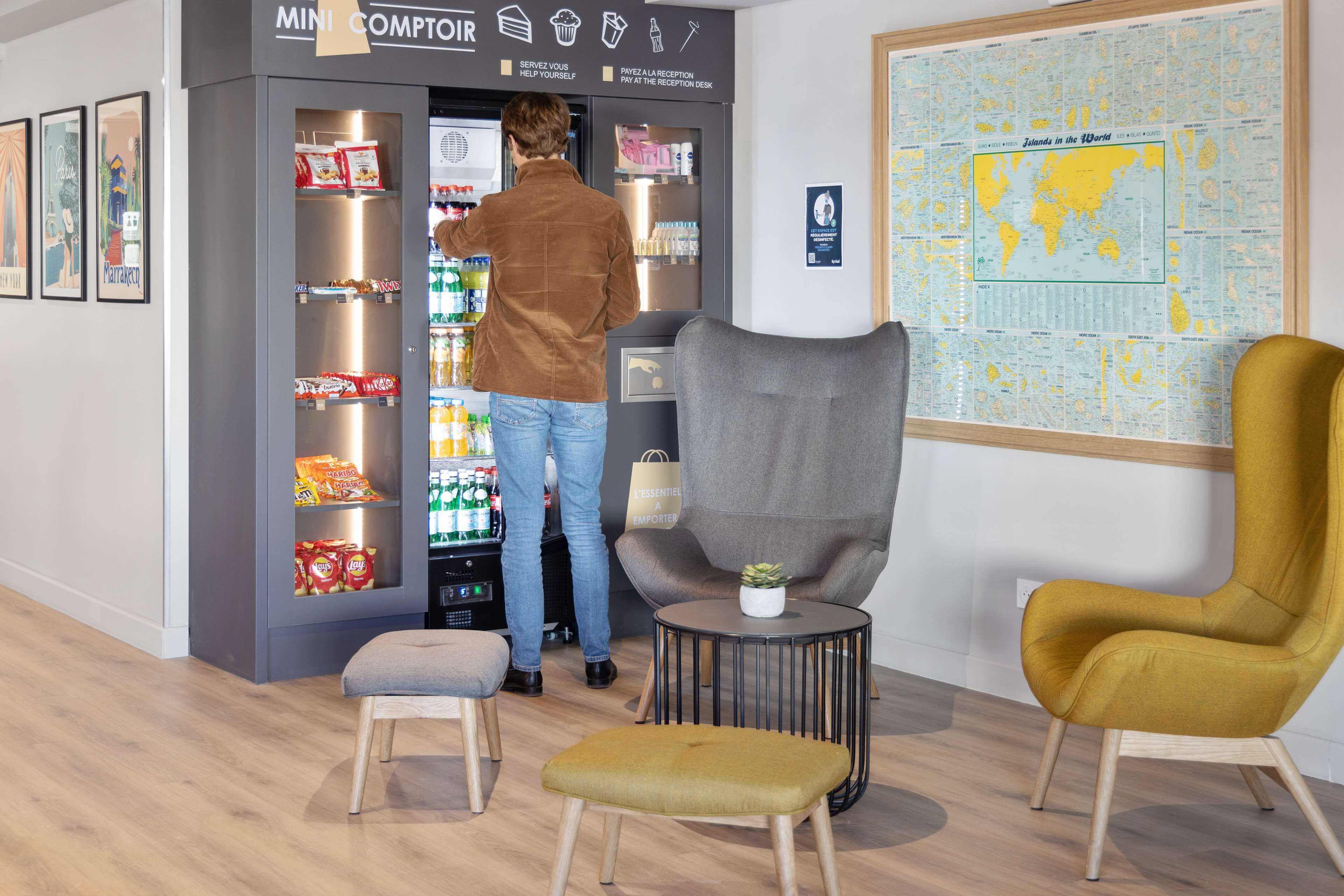 A man interacting with a vending machine in a modern interior with a map on the wall and stylish seating.