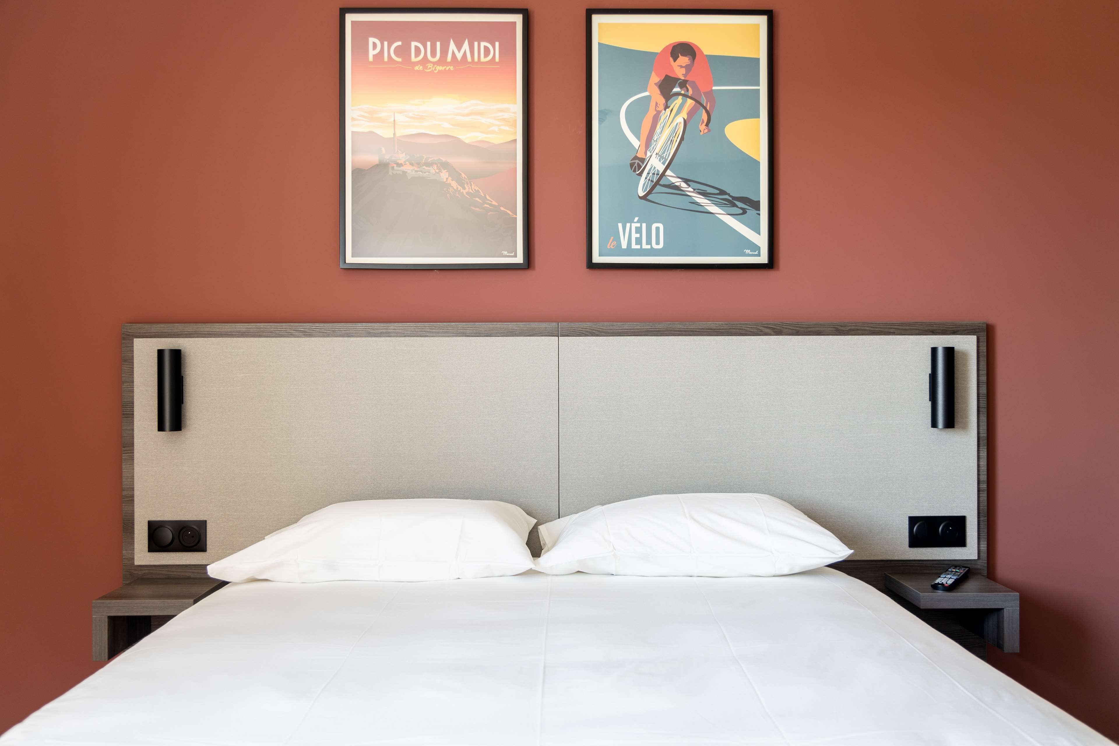 A neatly made bed with white linens, a headboard, and two wall-mounted nightstands with a remote control on one.