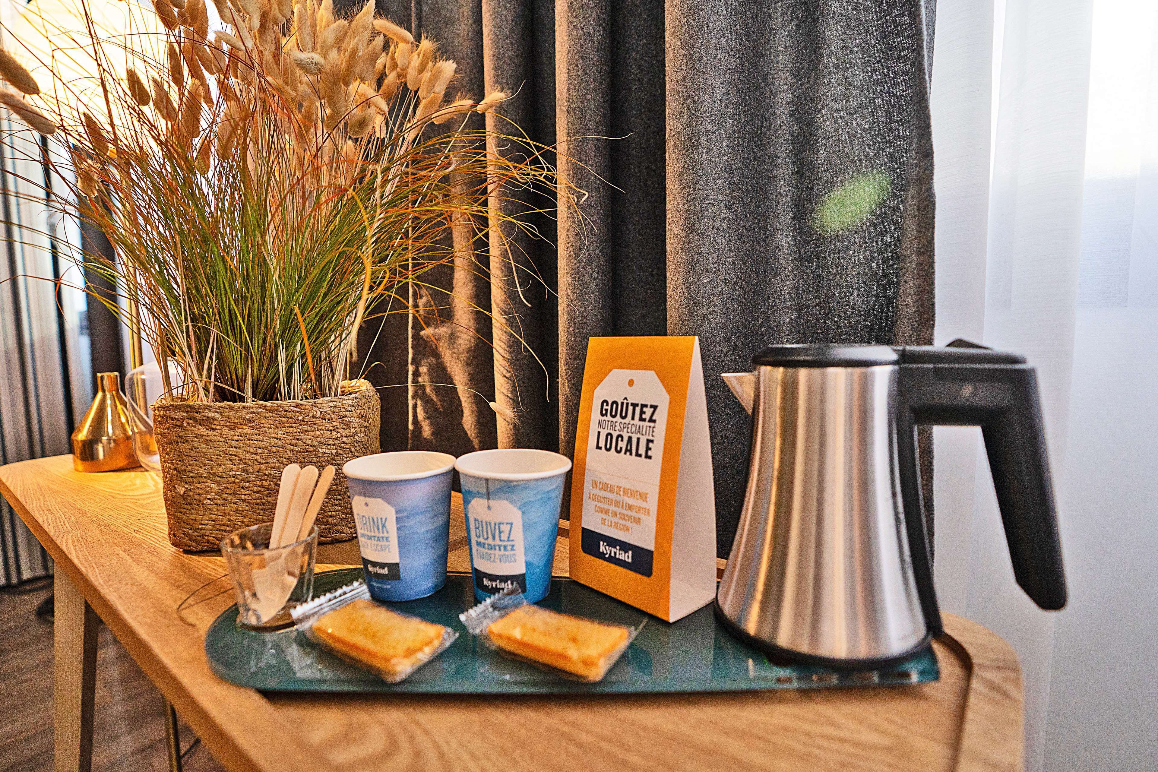 A breakfast setup with a coffee maker, two cups, a basket, and a tray with pastries.