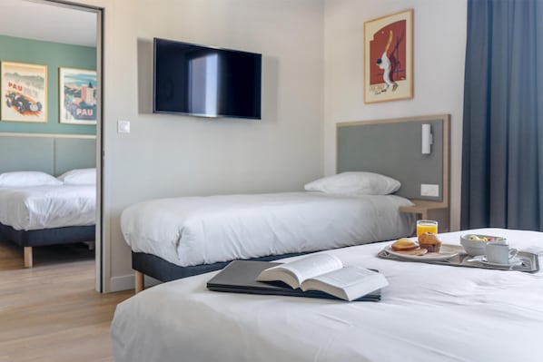 A hotel room with two beds, a flat-screen TV, artwork on the walls, and a breakfast tray on the bed.