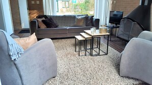 A modern living room with a grey sofa, two armchairs, a coffee table, and a TV. - Bungalow on vacation park near the beach Noordwijk (Noordwijkerhout)