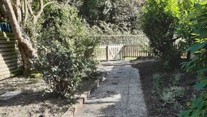 A gravel path leading to a wooden gate, surrounded by dense foliage and a wooden fence. - Bungalow on vacation park near the beach Noordwijk (Noordwijkerhout)