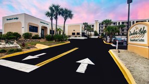 Een hotelentree met een bordje voor 'Bendini's Lodge Oceanfront Suites', een parkeerplaats met pijlen en palmbomen.