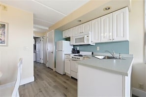 A kitchen with white cabinets, a microwave, a stove, and a sink.