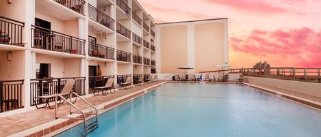 A multi-story hotel with a swimming pool, balconies, and sun loungers.
