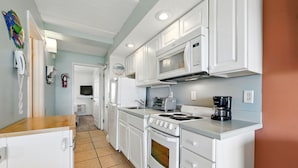 A kitchen with white cabinets, a stove, a microwave, and a coffee maker. - Beacher's Oceanfront Balcony Suite with onsite Front Desk and Staff (St. Augustine)