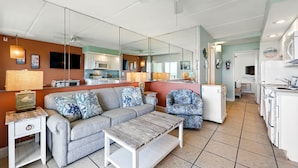 A modern living room with a grey sofa, a coffee table, and a mirrored wall reflecting the kitchen area. - Beacher's Oceanfront Balcony Suite with onsite Front Desk and Staff (St. Augustine)