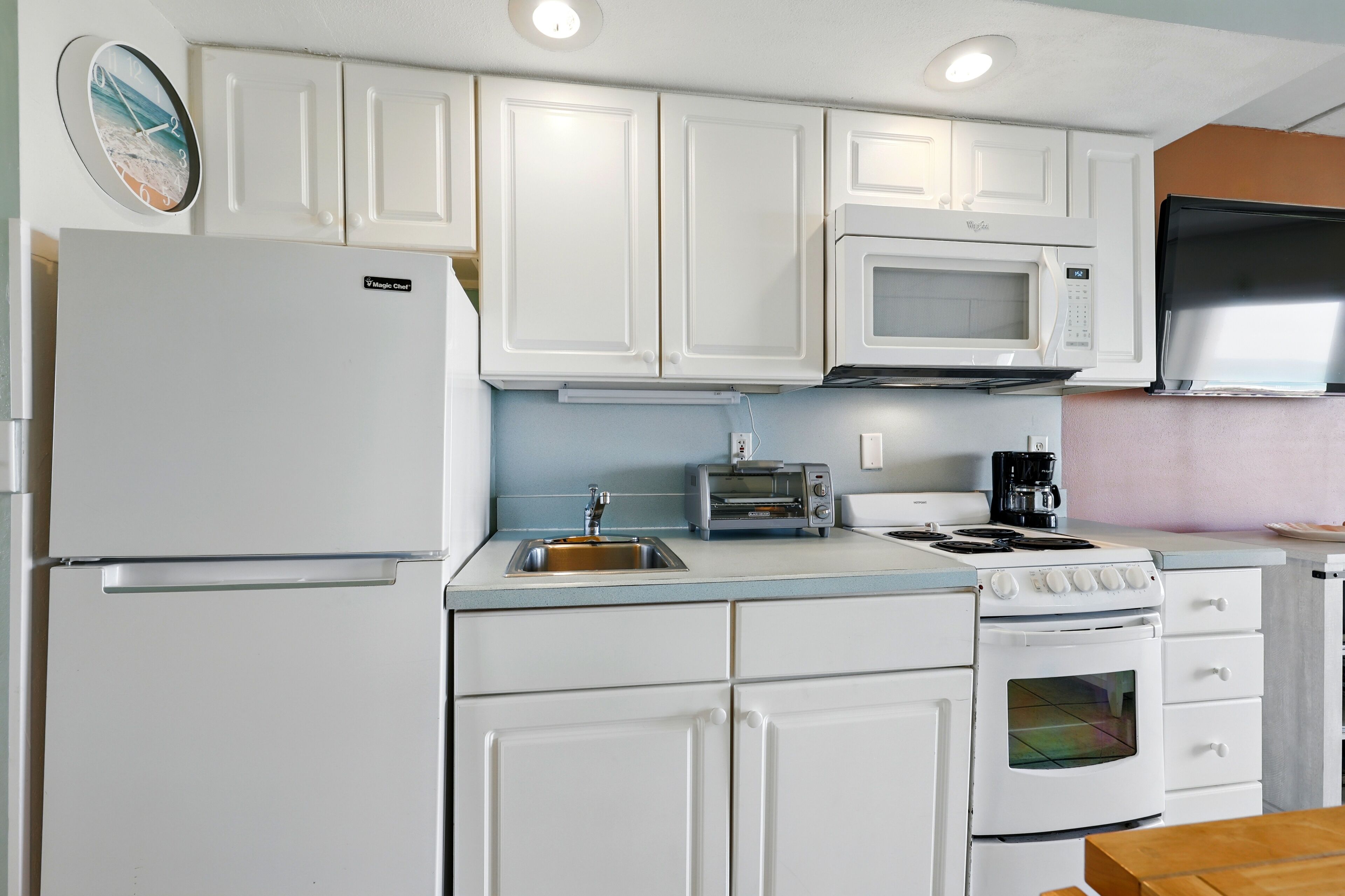 A compact kitchen with white cabinetry, a built-in microwave, a toaster, and a stove.