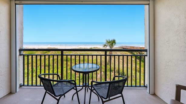 A balcony with a glass table and two chairs, overlooking a beach and ocean. - Beacher's Oceanfront Balcony Suite with onsite Front Desk and Staff (St. Augustine)