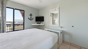 A bedroom with a large bed, a television, a mirror, and a view of the outdoors. - Beacher's Oceanfront Balcony Suite with onsite Front Desk and Staff (St. Augustine)