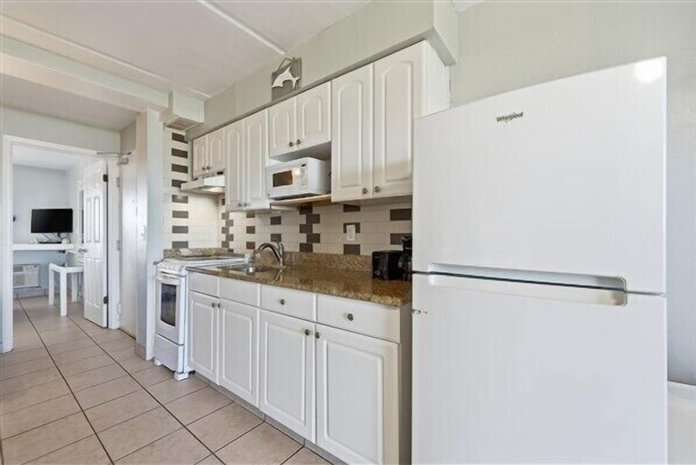 A modern kitchen with white cabinets, a built-in oven, and a refrigerator.