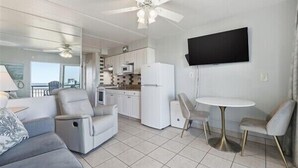 A modern living room with a sofa, a dining table with chairs, a kitchen area, and a TV mounted on the wall. - Beacher's Oceanfront Balcony Suite with onsite Front Desk and Staff (St. Augustine)