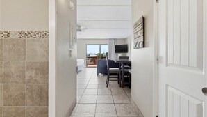Un couloir avec un sol carrelé, un coin repas avec des chaises et une table, un téléviseur et une porte.