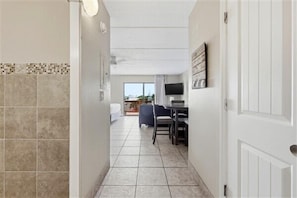 A hallway with tiled flooring, a dining area with chairs and a table, a television, and a door. - Beacher's Lodge Studio Suite Plus with onsite Front Desk and Staff (St. Augustine)