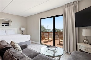 A hotel room with a bed, a sofa, a glass table, a TV, and a balcony with a view.