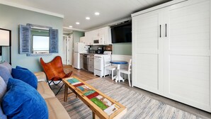 Un espacio habitable compacto con kitchenette, comedor y zona de estar con sofá y sillones.