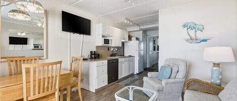 Una sala de estar moderna con comedor, cocina y televisor montado en la pared.