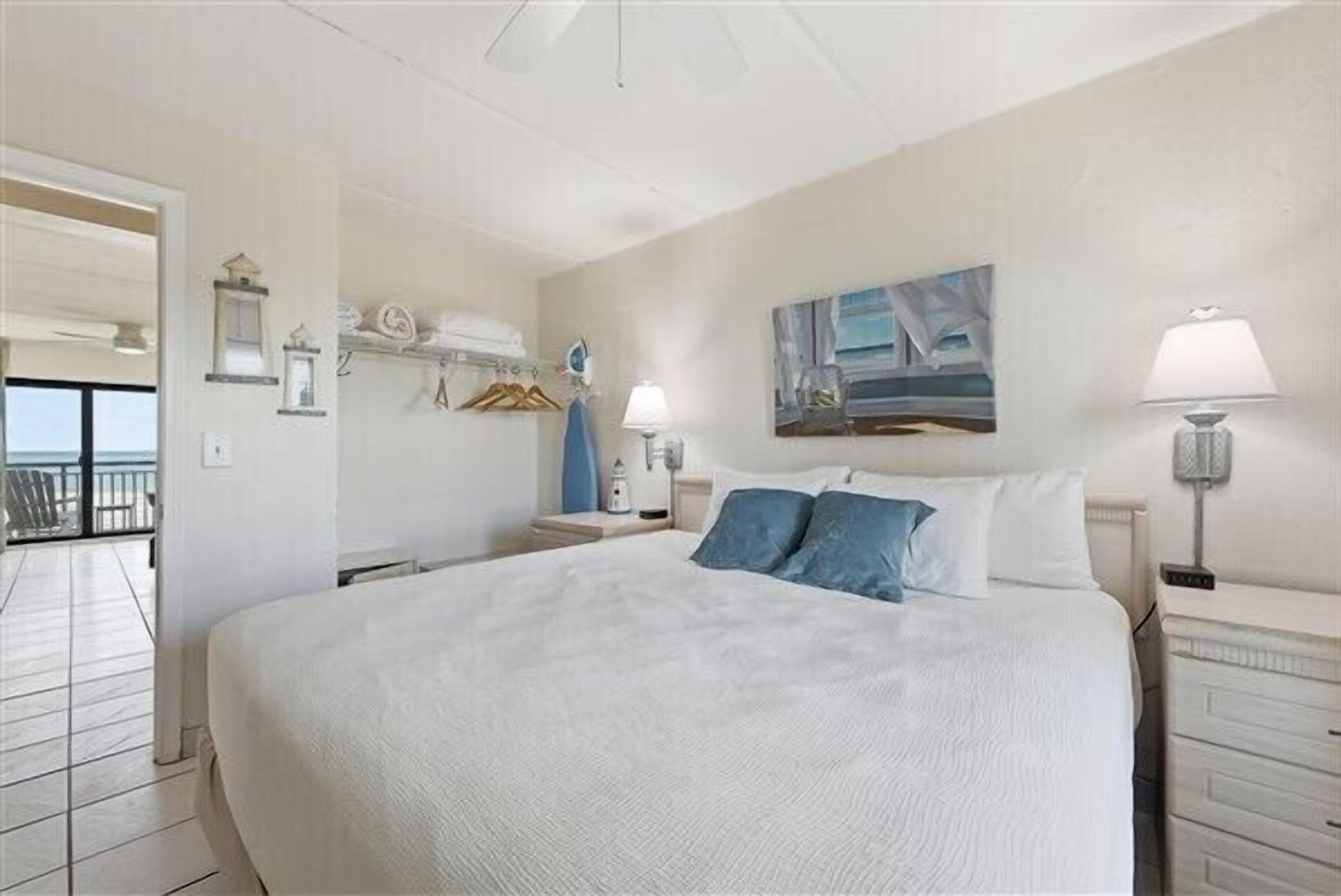 A bedroom with a large bed, a painting on the wall, and a balcony visible through an open door.