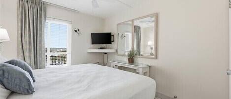 A hotel room with a bed, a television, a mirror, a ceiling fan, and a window with curtains.