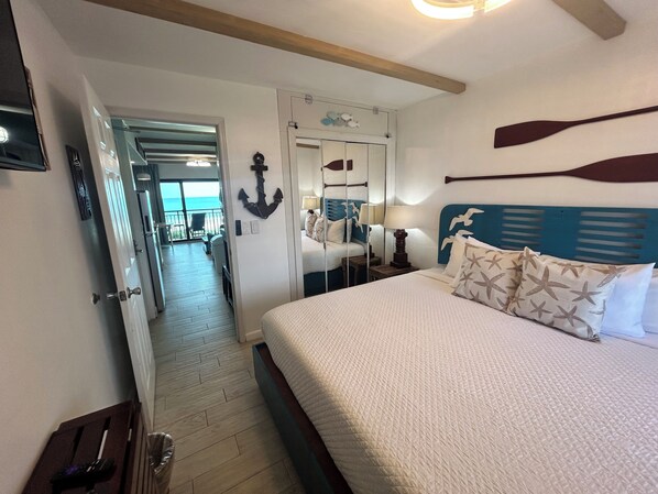 Habitación de hotel con cama, mesita de noche, espejo y vista al mar a través de una puerta.