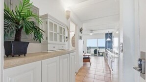 Une cuisine lumineuse avec des meubles blancs, une plante en pot et une vue sur un balcon.