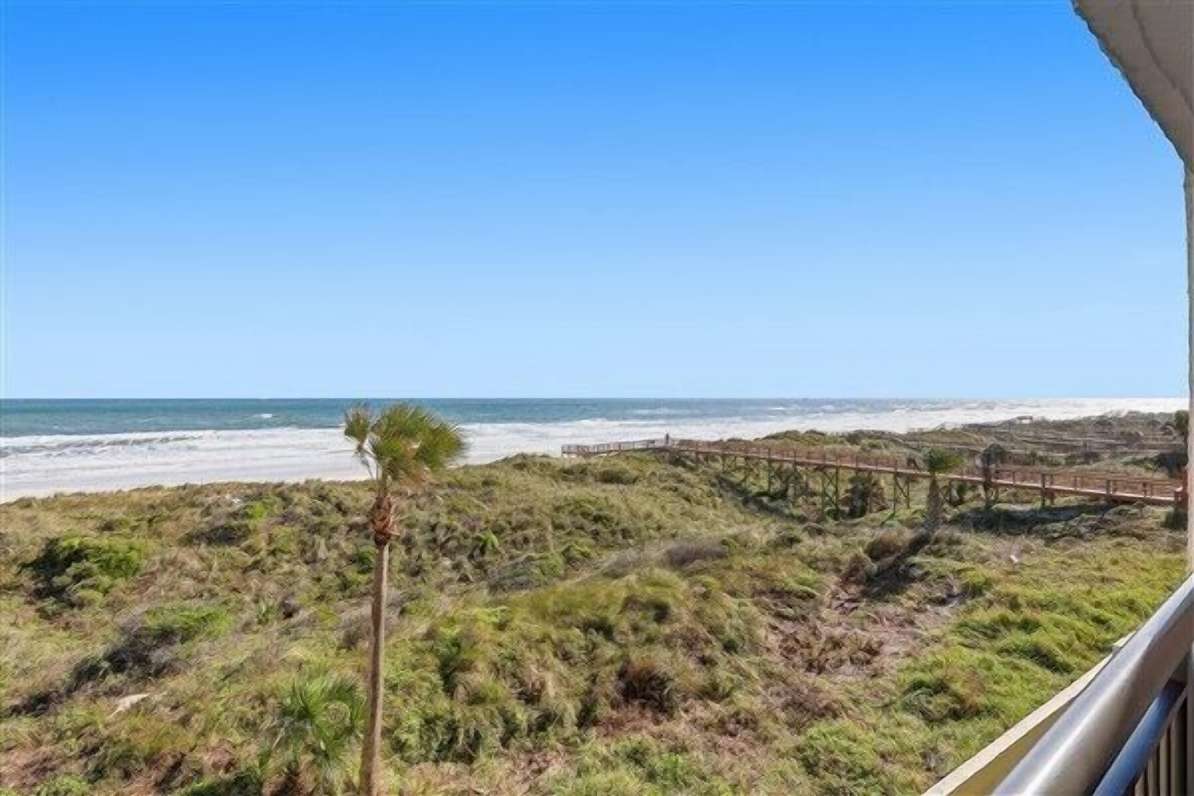 Vista a la playa con un paseo marítimo de madera y vegetación escasa.